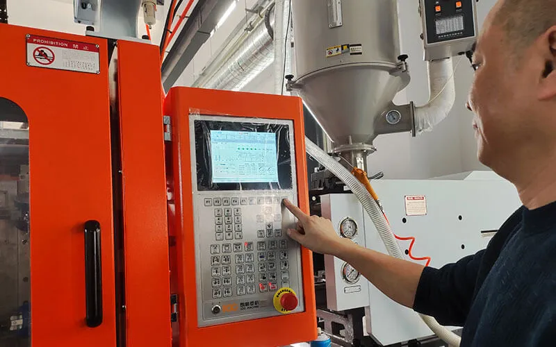 Worker operates automatic injection molding machine control panel for plastic glue cartridge production